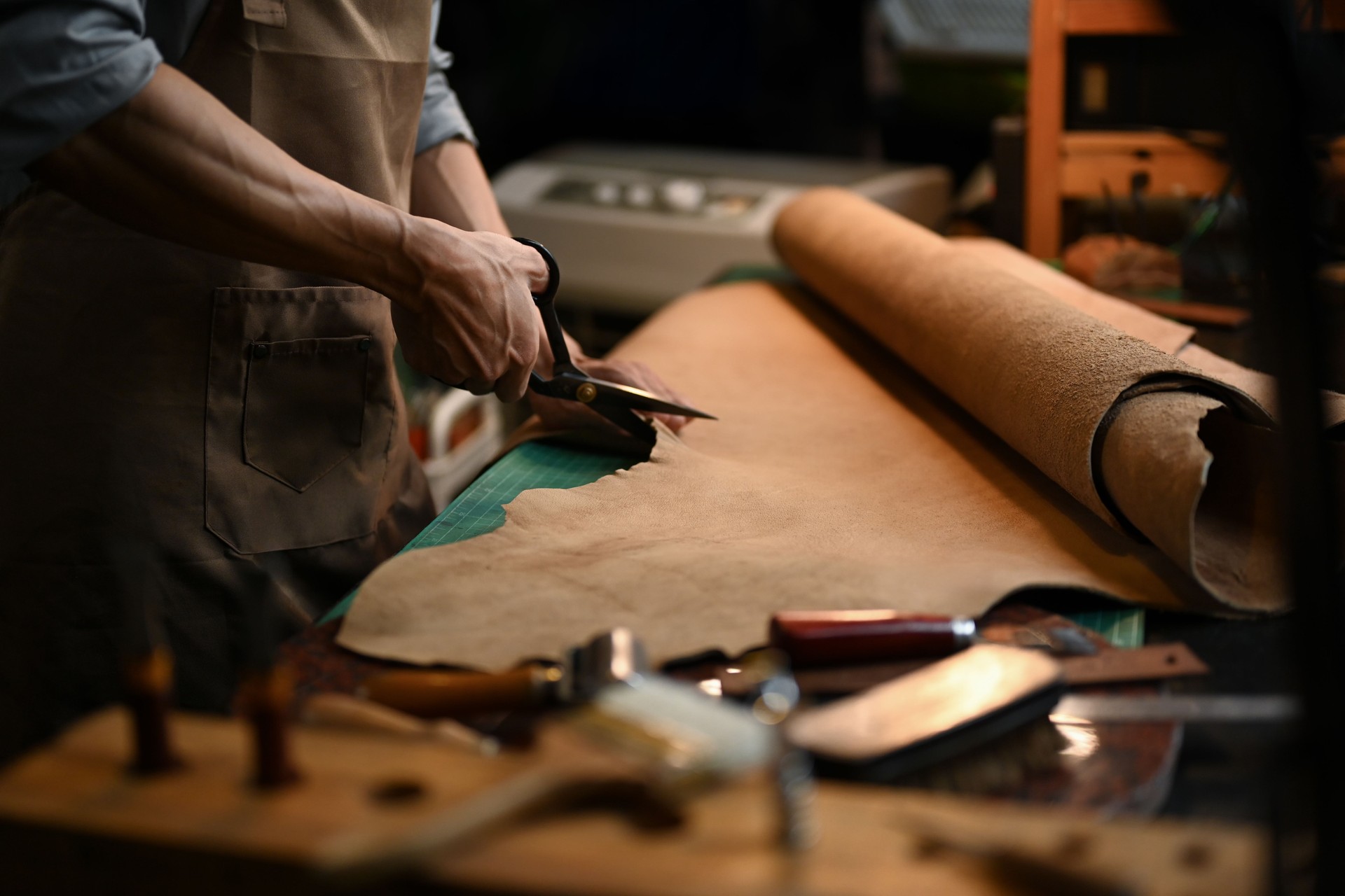 Cropped shot of a craftsman cutting a large piece of leather with precision scissors in his workshop