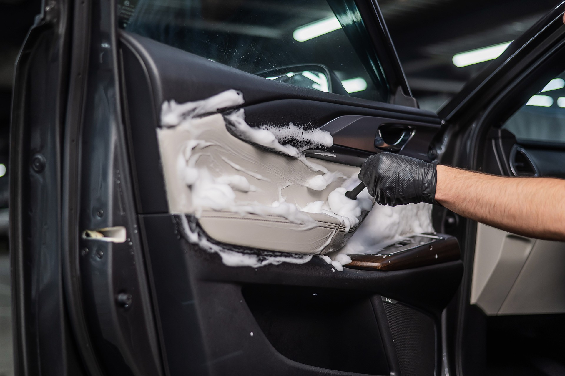 A man cleans the interior of a car with foam and a brush. Clean the door trim.